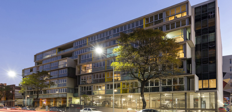 exterior up-shot of iStay Precinct hotel in Adelaide city at dusk with lights on and car parking on street